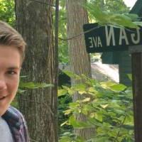 Mack smiling, standing among trees in front of a sign that says Michigan Avenue